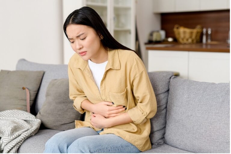 A woman sitting on the sofa is suffering from menstrual cramps and constipation