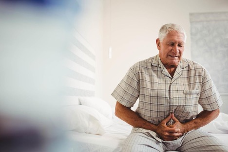 An elderly man in the bedroom is clutching his stomach experiencing the pain of colon cancer