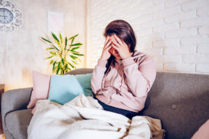 Woman having headache while sitting on sofa at home.